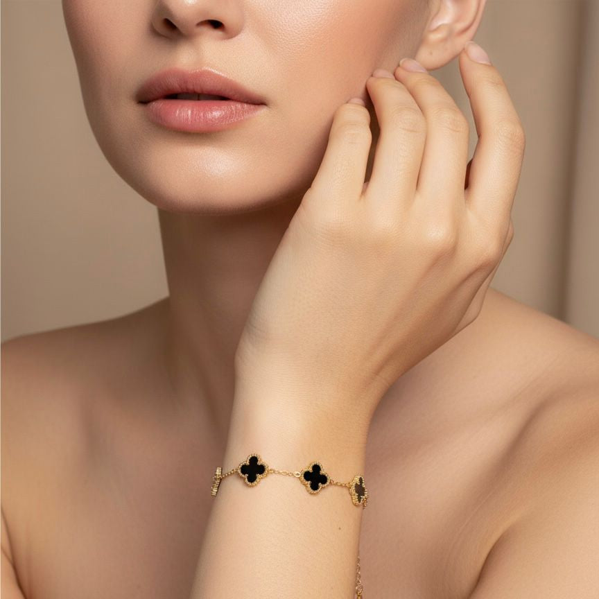 Gold bracelet with clover designs on a model's wrist against a neutral background
