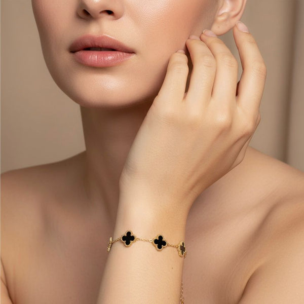Gold bracelet with clover designs on a model's wrist against a neutral background
