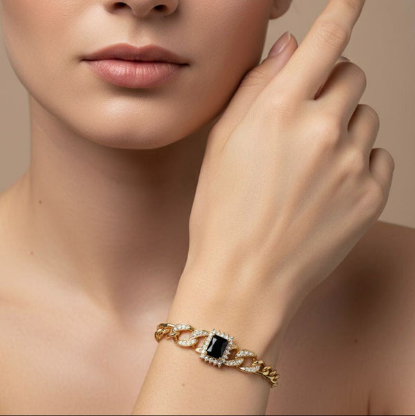 Gold bracelet with a black gemstone worn by a model against a neutral background